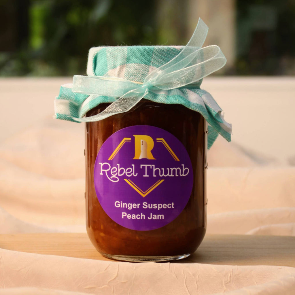 California made jar of Rebel Thumb organic Ginger Suspect Peach Jam with a turquoise ribbon on a beige surface.