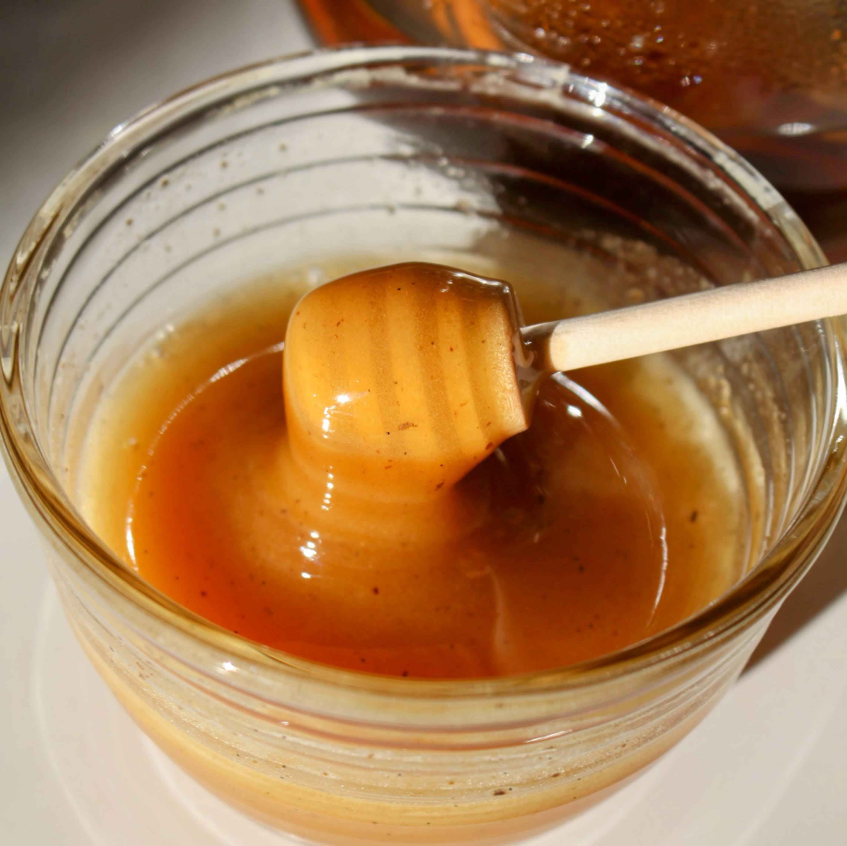 Glass bowl of Rebel Thumb Local Artisan Wildflower Honey made in California with a wooden honey dipper