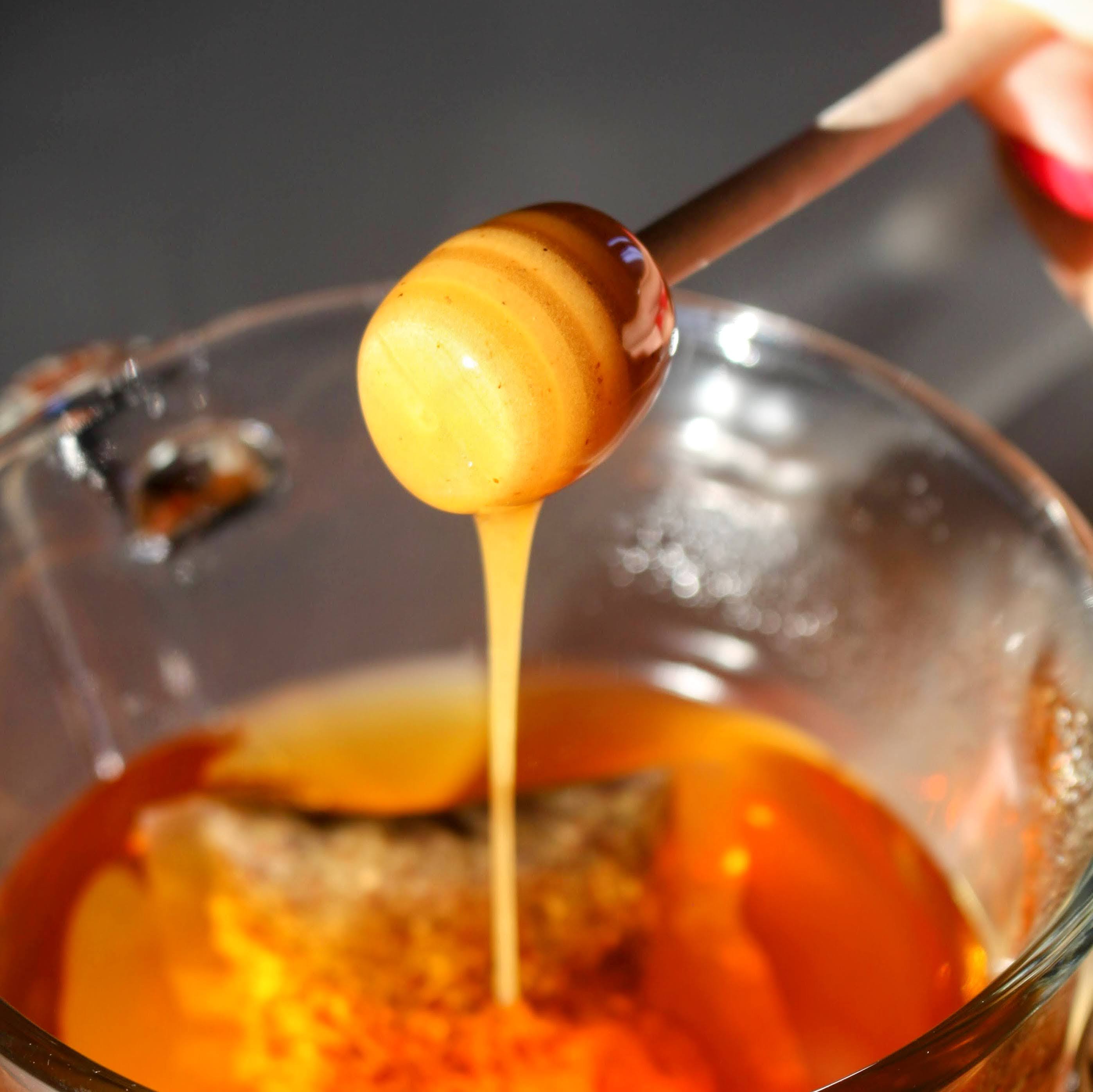 Drizzle of Rebel Thumb Local Artisan Wildflower Honey made in California being poured in tea with a wooden honey dipper